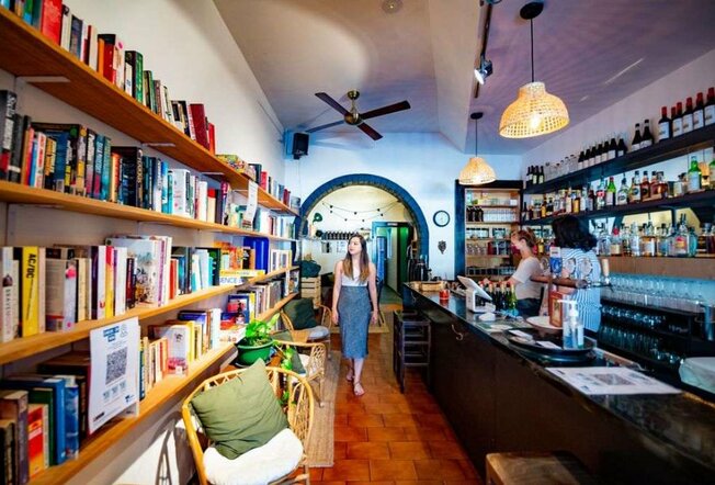 A woman walking through a wine bar with a bookshelf.
