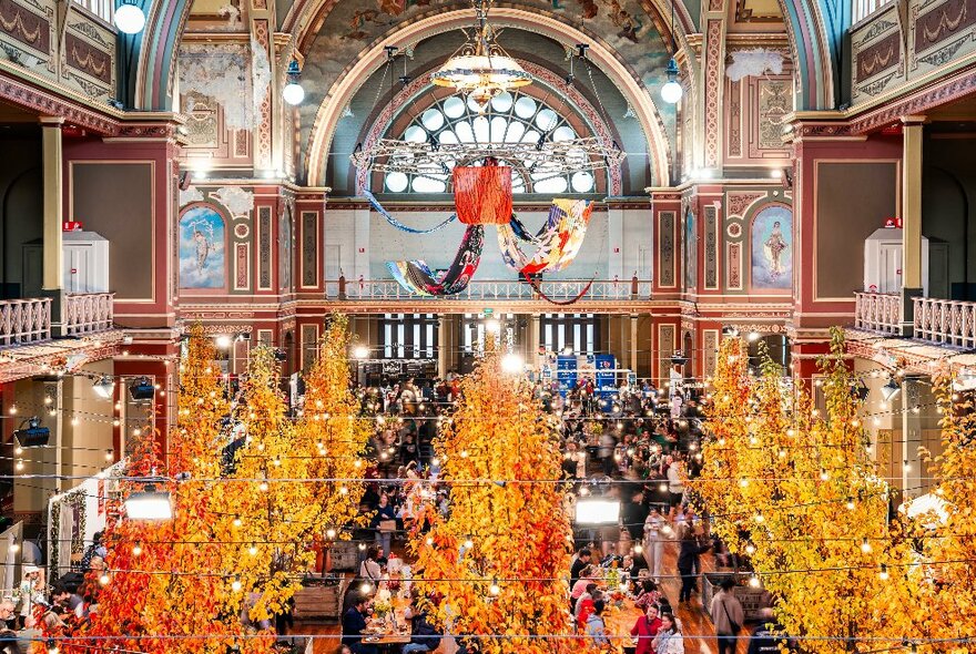 The interior of Royal Exhibition Building with autumn decorations and crowds of people milling around the indoor market stalls. 