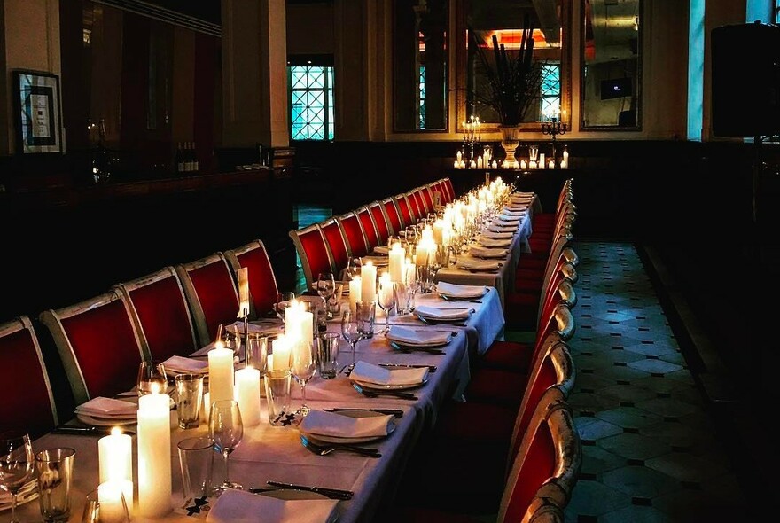 Long restaurant table with lit candles on it and two long rows of red chairs.