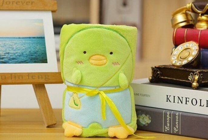 A green stuffed toy surrounded by a stack of books, a phone and a painting