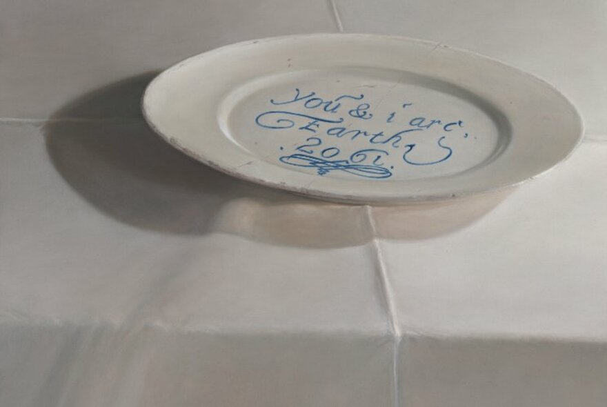 A white ceramic dinner plate with a blue inscription, on a white table.