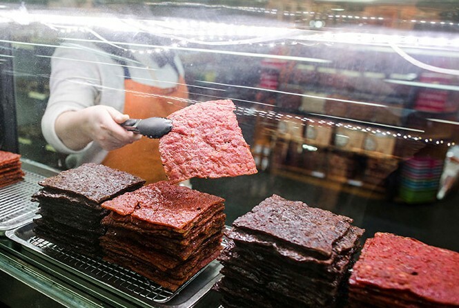 Staff member using tongs to pick up a square of jerky from one of four stacks of jerky.