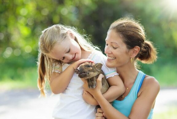 Smiling woman and young child patting a piglet they hold in their arms.