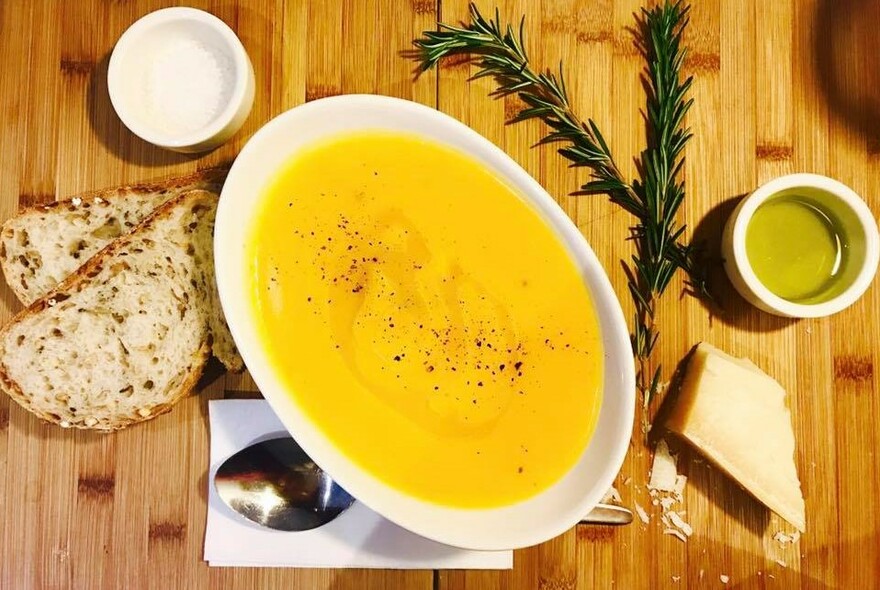 Oval dish of pumpkin soup with bread and condiments.
