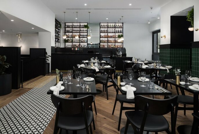 A chic restaurant interior with black dining tables and chairs and a bar in the background