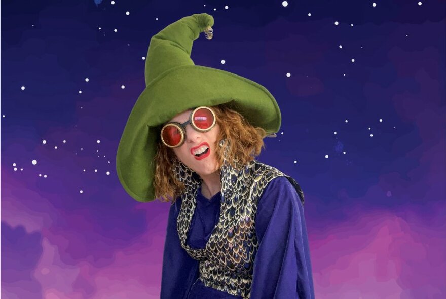 A wizard performer wearing a big green hat and glasses, against a purple starry sky.