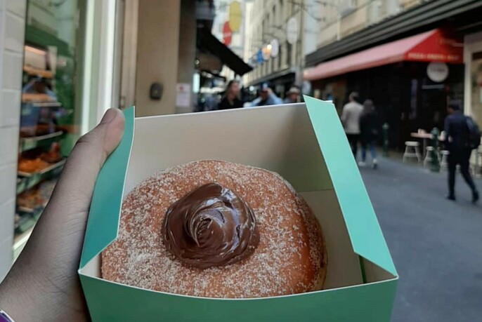 Chocolate-filled donut being held up in a green box, with laneway in background.