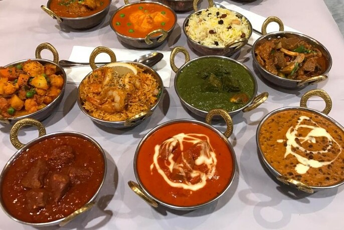 Array of curries in silver bowls with handles, including rice, dhal and stews.