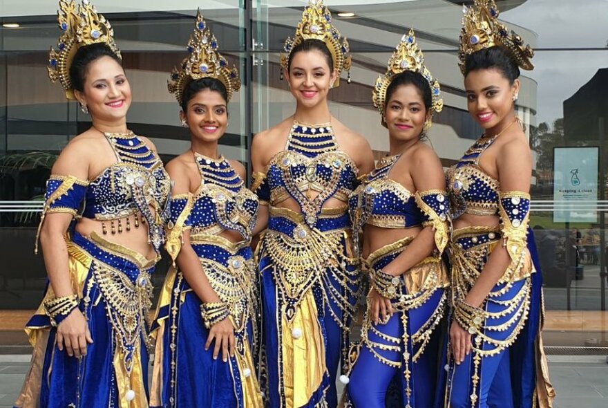 Five women standing together in a line, dressed in blue and gold traditional Sri Lankan dancing costumes, smiling at the camera.