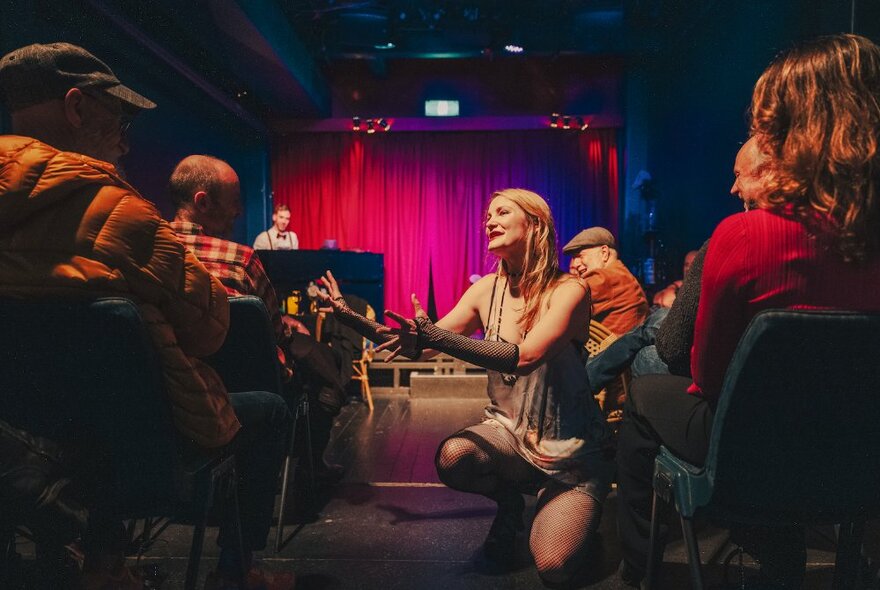 A woman kneels to the audience while performing in a cabaret setting