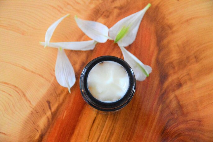 Flower petals surrounding a round black bowl of cleansing cream.