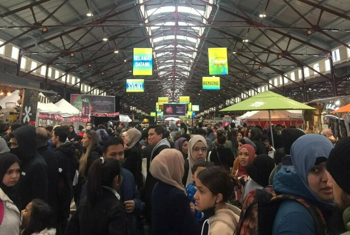 A large crowd of people in an undercover shed aisle at Queen Victoria Market.