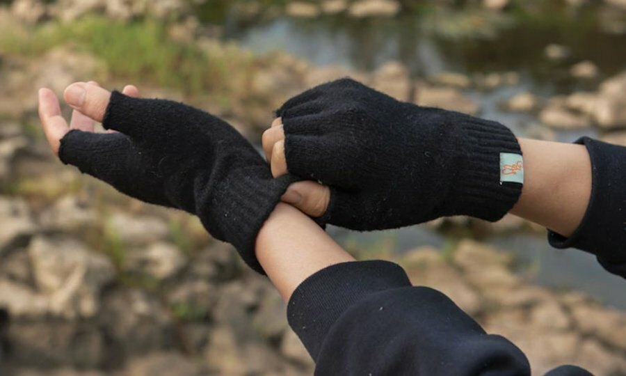 Close up of person putting on black fingerless gloves. They are outside in a park and using one hand to pull the gloves over the other.