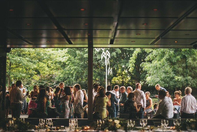Crowd of people standing in a cafe that overlooks greenery and trees.