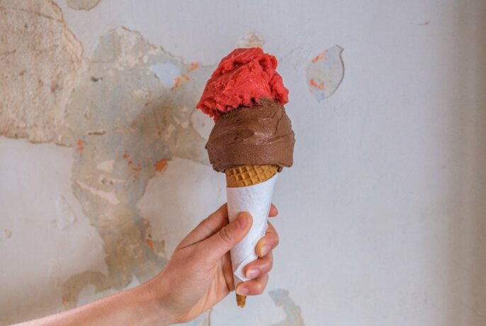 A hand holding an ice cream cone with a pink scoop and a chocolate scoop.