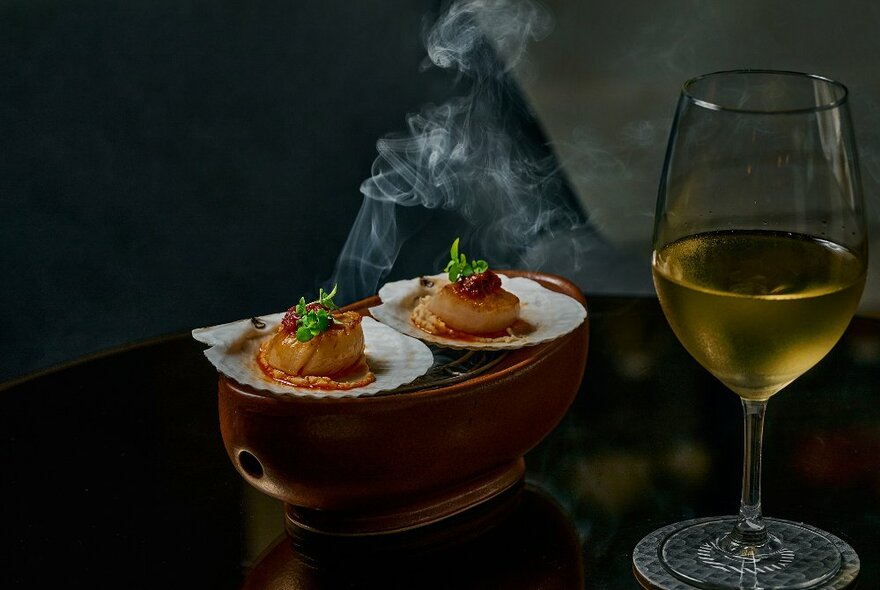 Two steaming-hot plates of food on a display next to a glass of white wine.