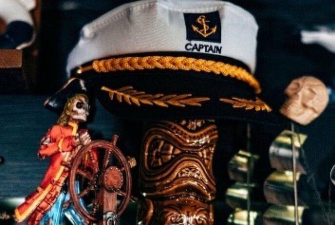 Captain's cap propped on a ceramic tiki vessel, with other nautical decorations alongside.