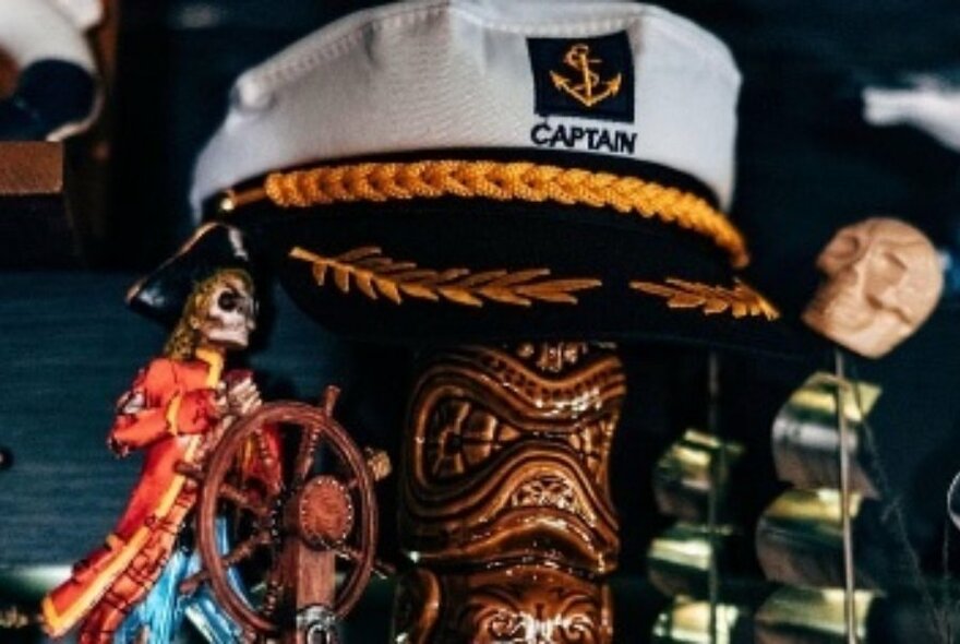 Captain's cap propped on a ceramic tiki vessel, with other nautical decorations alongside.