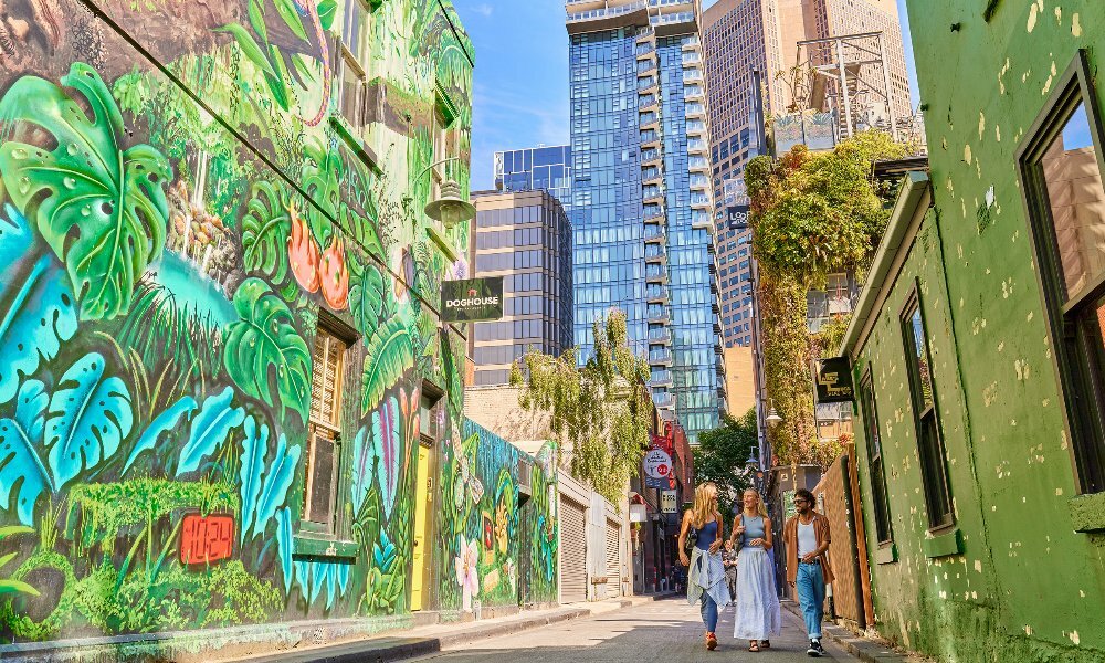 Three friends are walking down an alley way with jungle-themed street art on the walls
