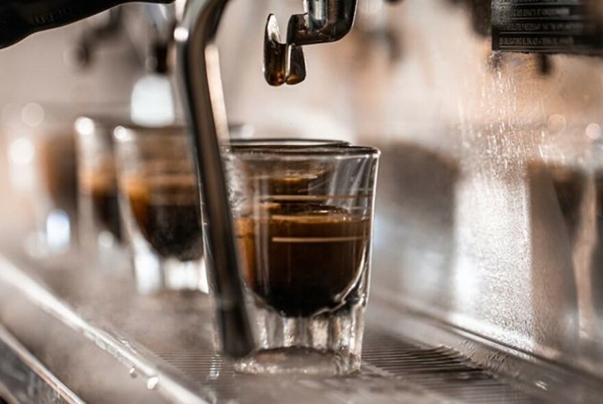 Espresso glasses being filled with coffee from a coffee machine.