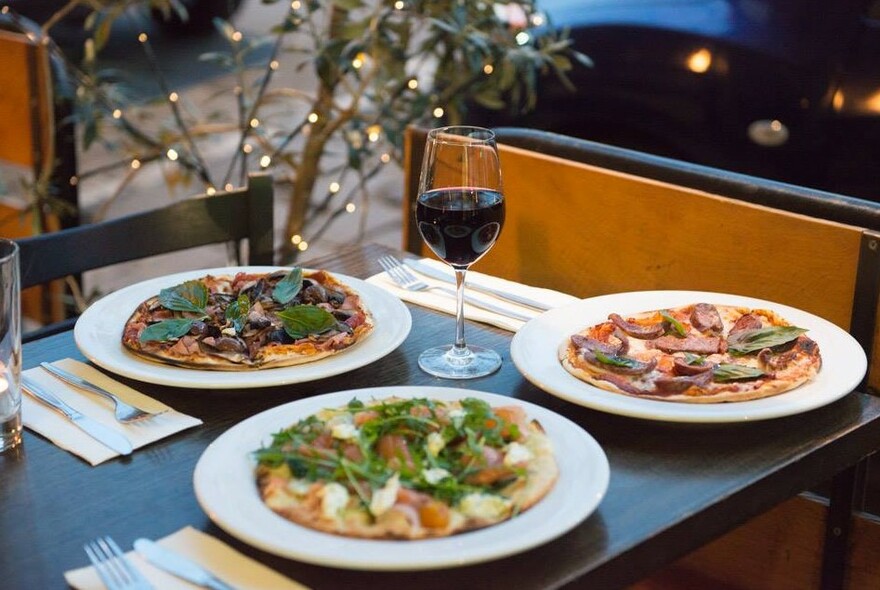 Table with three pizzas and a glass of red wine.