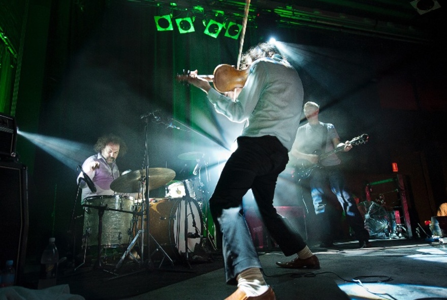 The band, The Dirty Three, performing on stage backlit by green-toned stage lights.