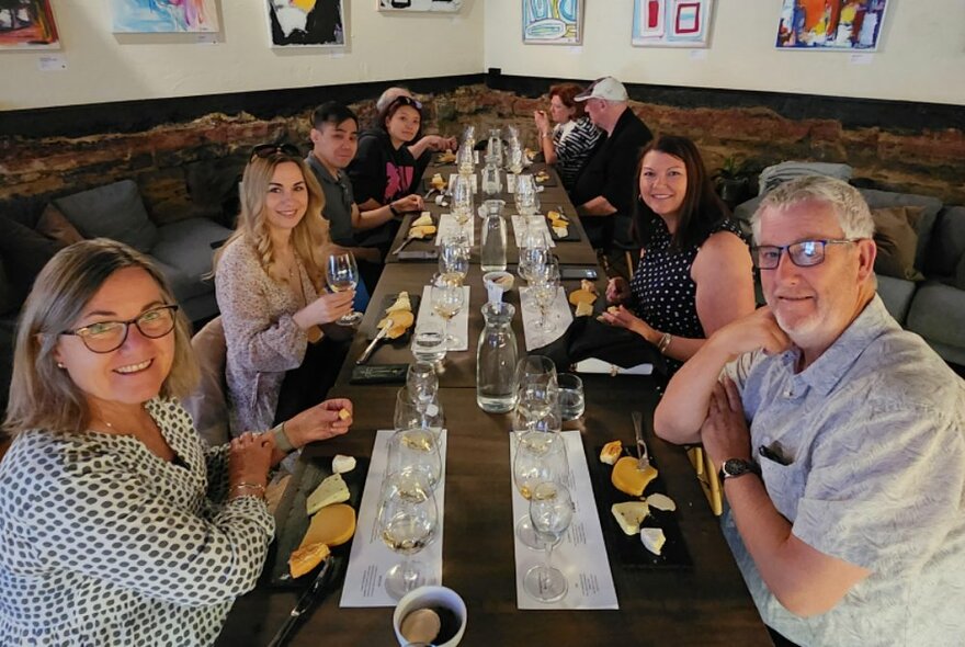People seated at a long table set with glasses and cheese in a restaurant setting.