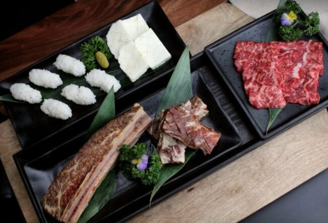 Cuts of meat and sushi rice on black plates.