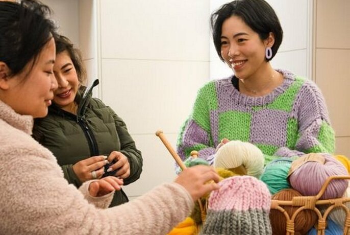 People sitting at a table with balls of wool and knitting needles.