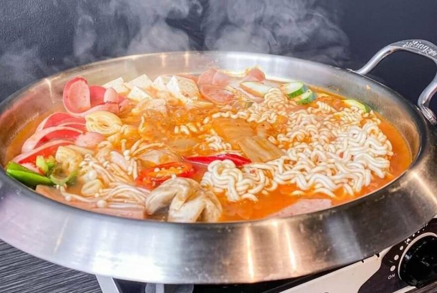 A bubbling and steaming hot-pot filled with broth, vegetables and noodles.