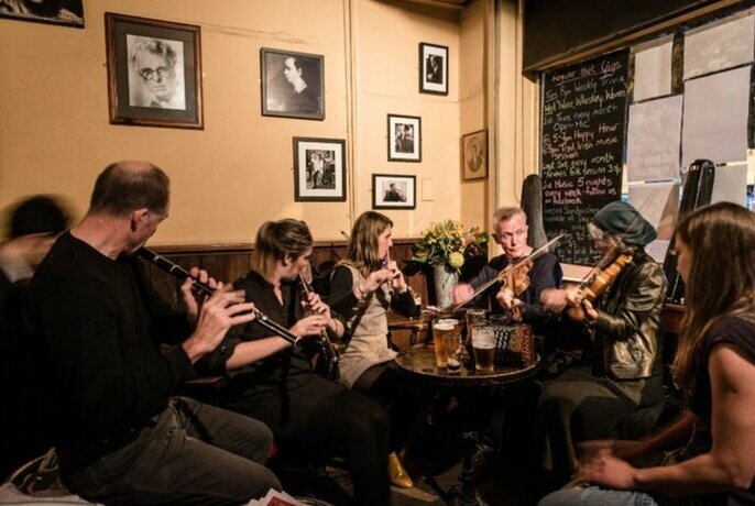 Several musicians playing instruments, seated around a small table inside a pub.
