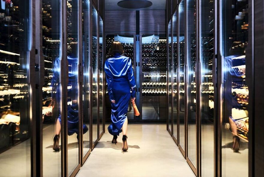 A woman walking through a contemporary wine cellar in a blue dress.