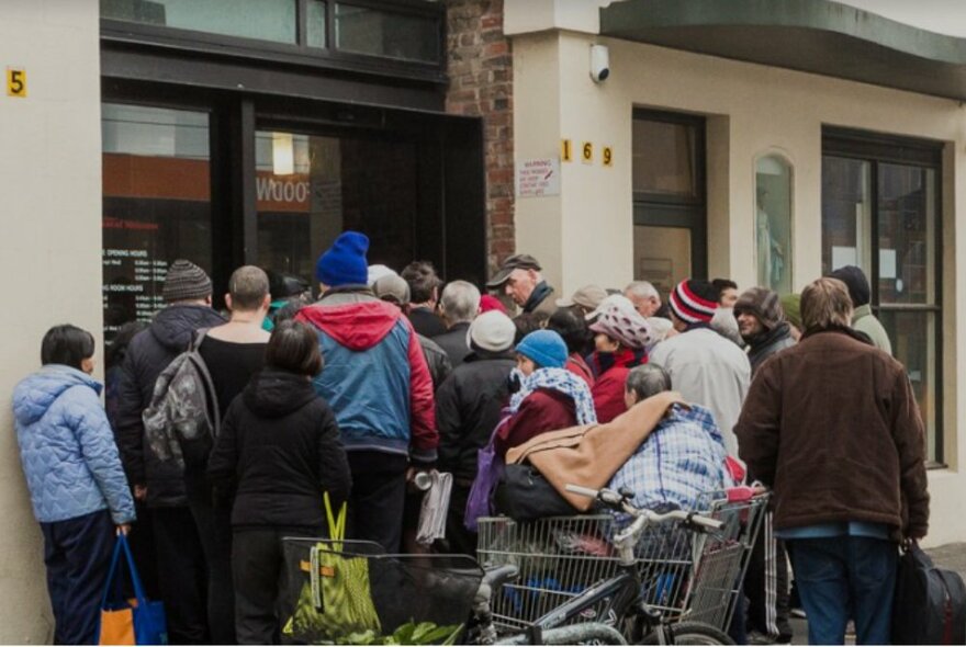 Homeless people with trolleys and bags waiting to enter a streetfront terrace premises.