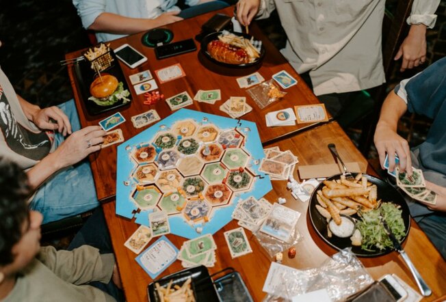 A group playing Settlers of Catan at a dining table with pub food. 