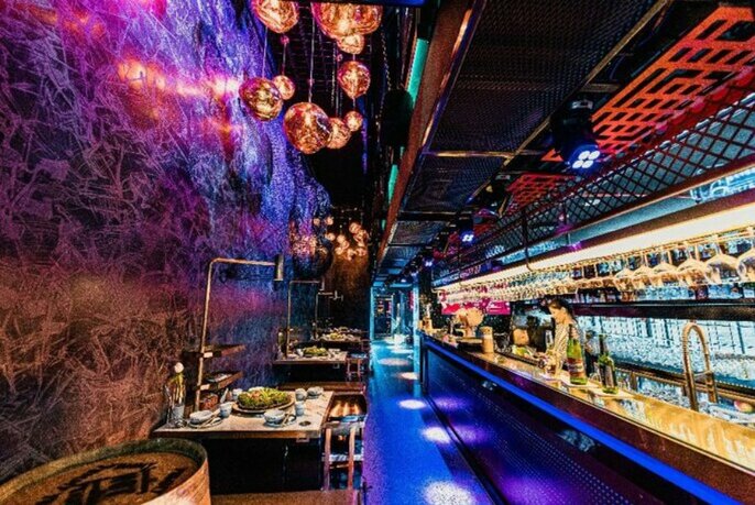 A trendy restaurant with purple lighting, a bar and pendant lighting. 