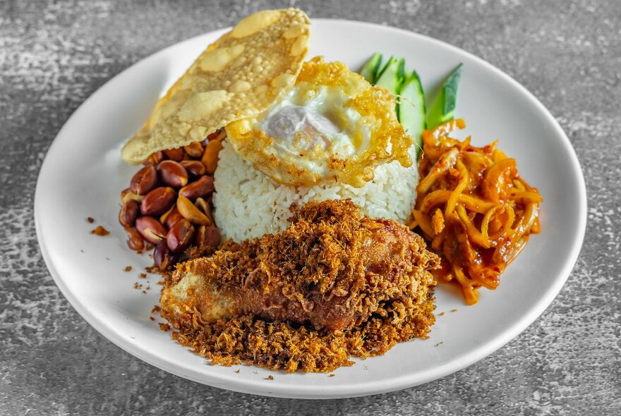 A round plate of Asian rice with a fried egg, crumbed cutlet and vegetables.