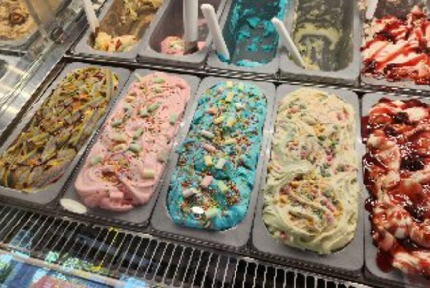 A selection of colourful gelato tubs in a fridge each with toppings.
