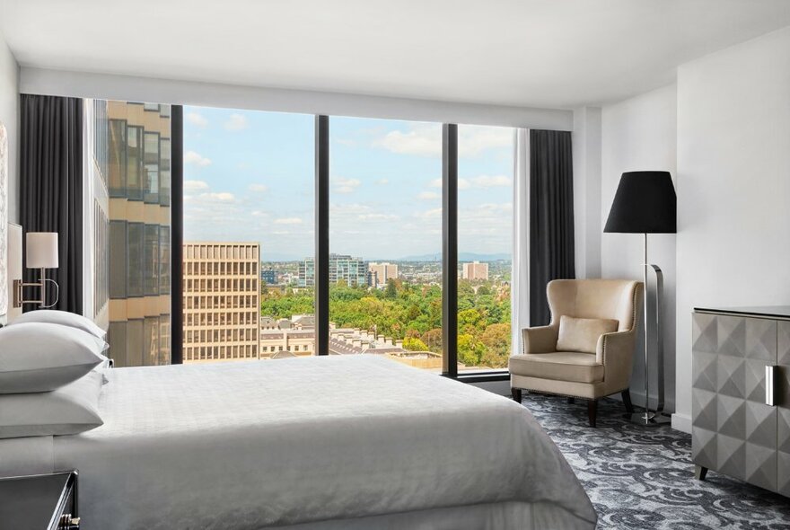 Hotel room with floor to ceiling windows with city and parkland views, decorated with simple but classic furnishings.
