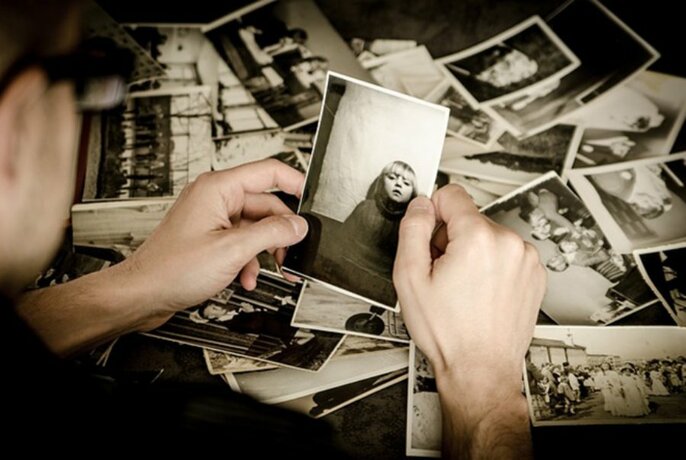 Overhead view of a pair of hands sorting through a large collection of old black and white photographs spread out over a table.