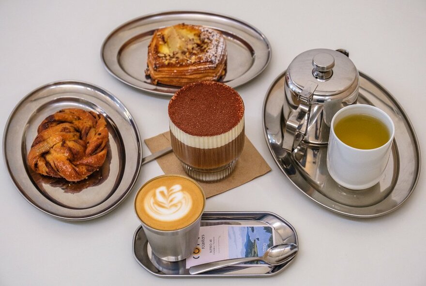 A table set with a latte, a layered dessert coffee, tea and pastries.