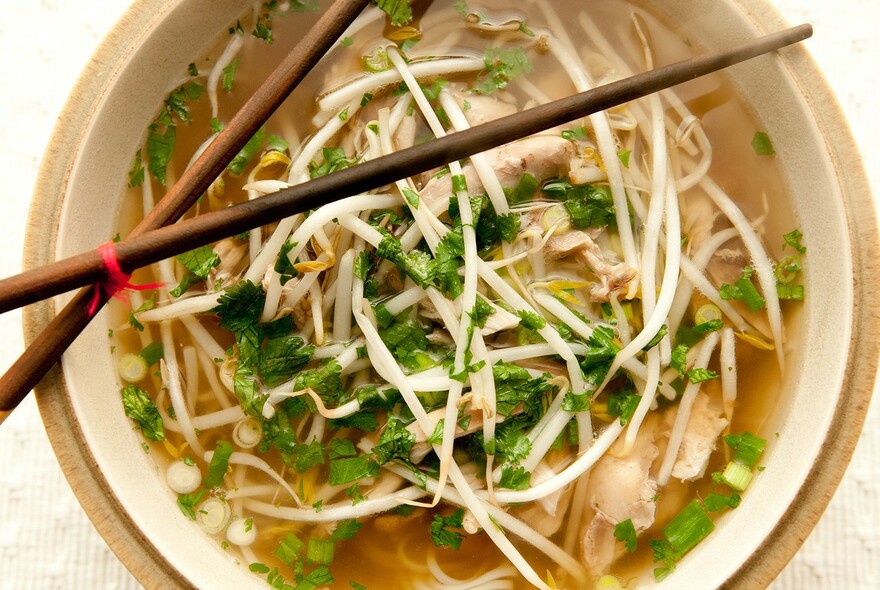 Round bowl of pho topped with bean sprouts, chopsticks balanced on top.