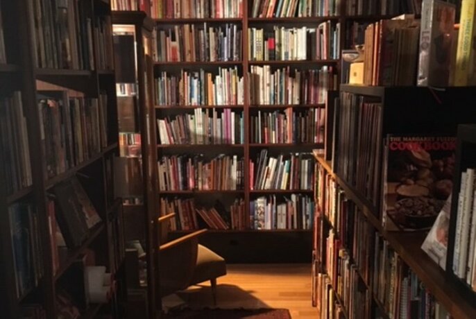 Atmospheric bookshop interior with shelves lined with books and light falling onto an armchair.