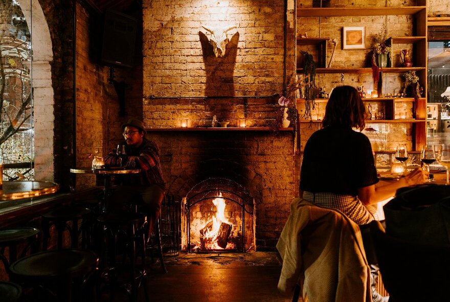 A fireplace in old building with peple at a bar. 