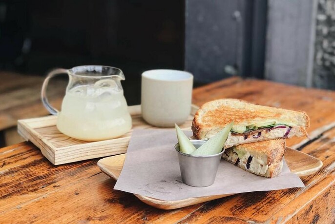 Wooden table with toasted sandwich, cup and glass jug on platters.