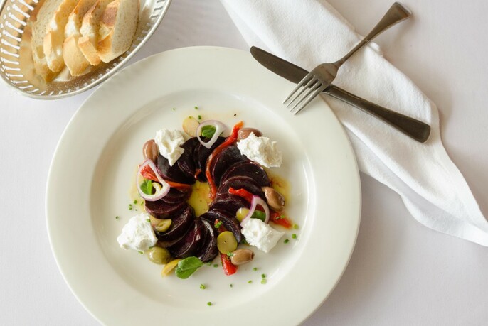 White plate of beetroot salad with bread and cutlery.