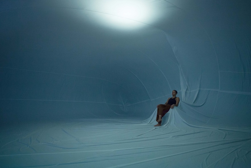 A dancer leaning back into a chair inside a giant white inflatable.