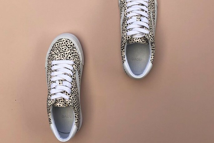 A pair of dotty laced sneakers viewed from above on a beige background.