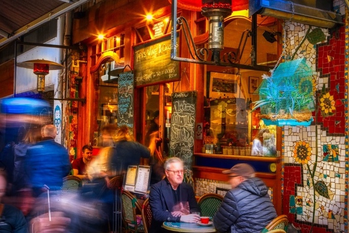A blurred motion image of people sitting at a table in a vividly decorated cafe.