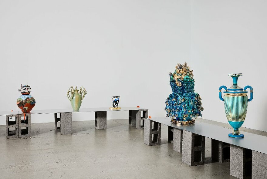 Five ornate ceramic sculptures on display on a low table in a white gallery space.
