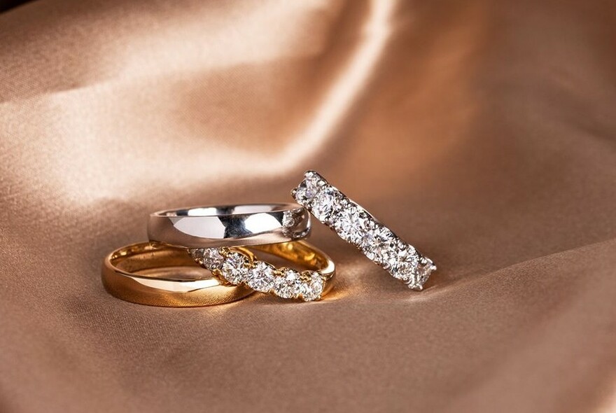 Four gold rings, two encircled with diamonds, on apricot silk cloth.